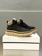 Lace-up sneakers on box: dark upper with beige collar and cream sole edge.