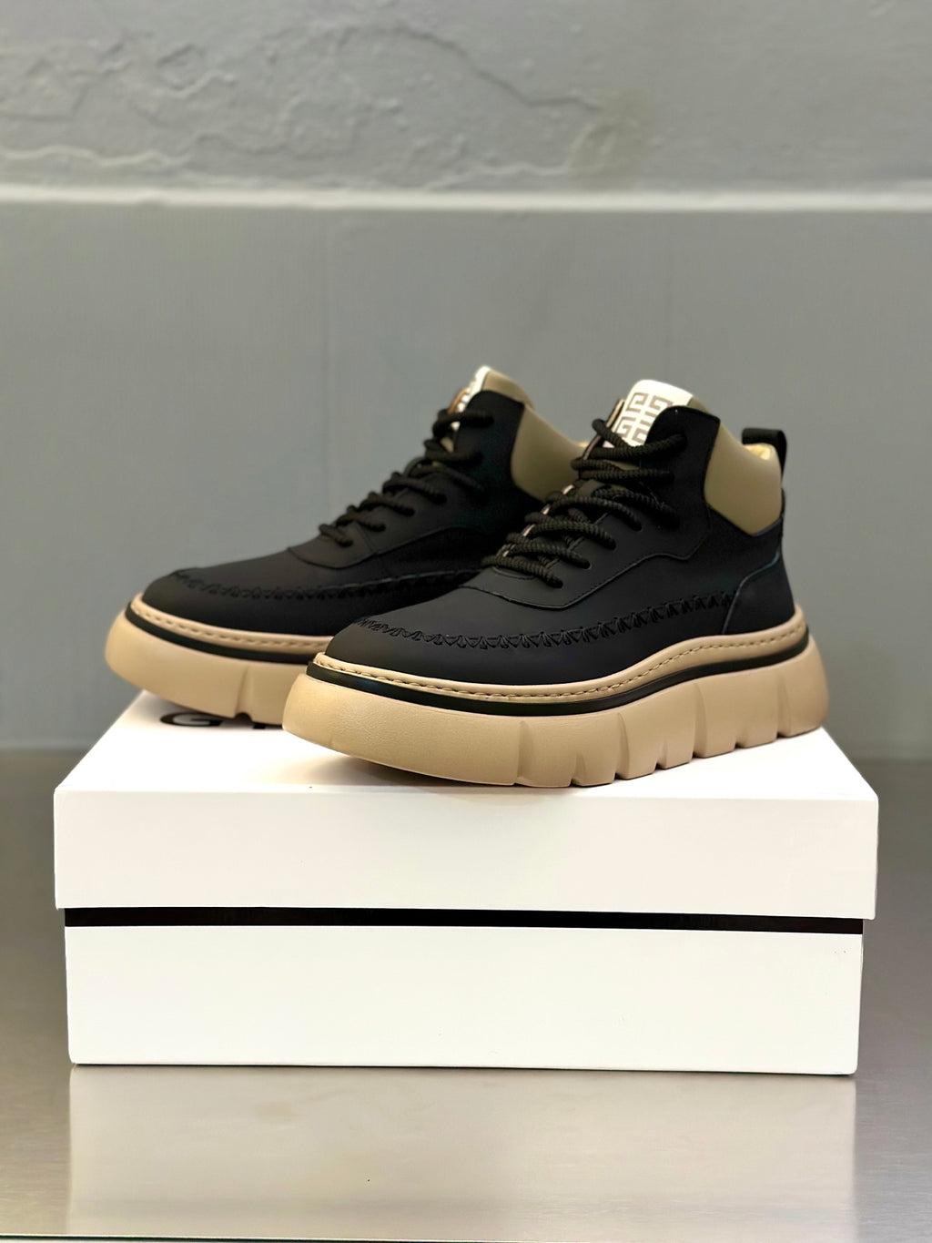Dark sneakers on a box, with thick beige platform sole and lace-up design