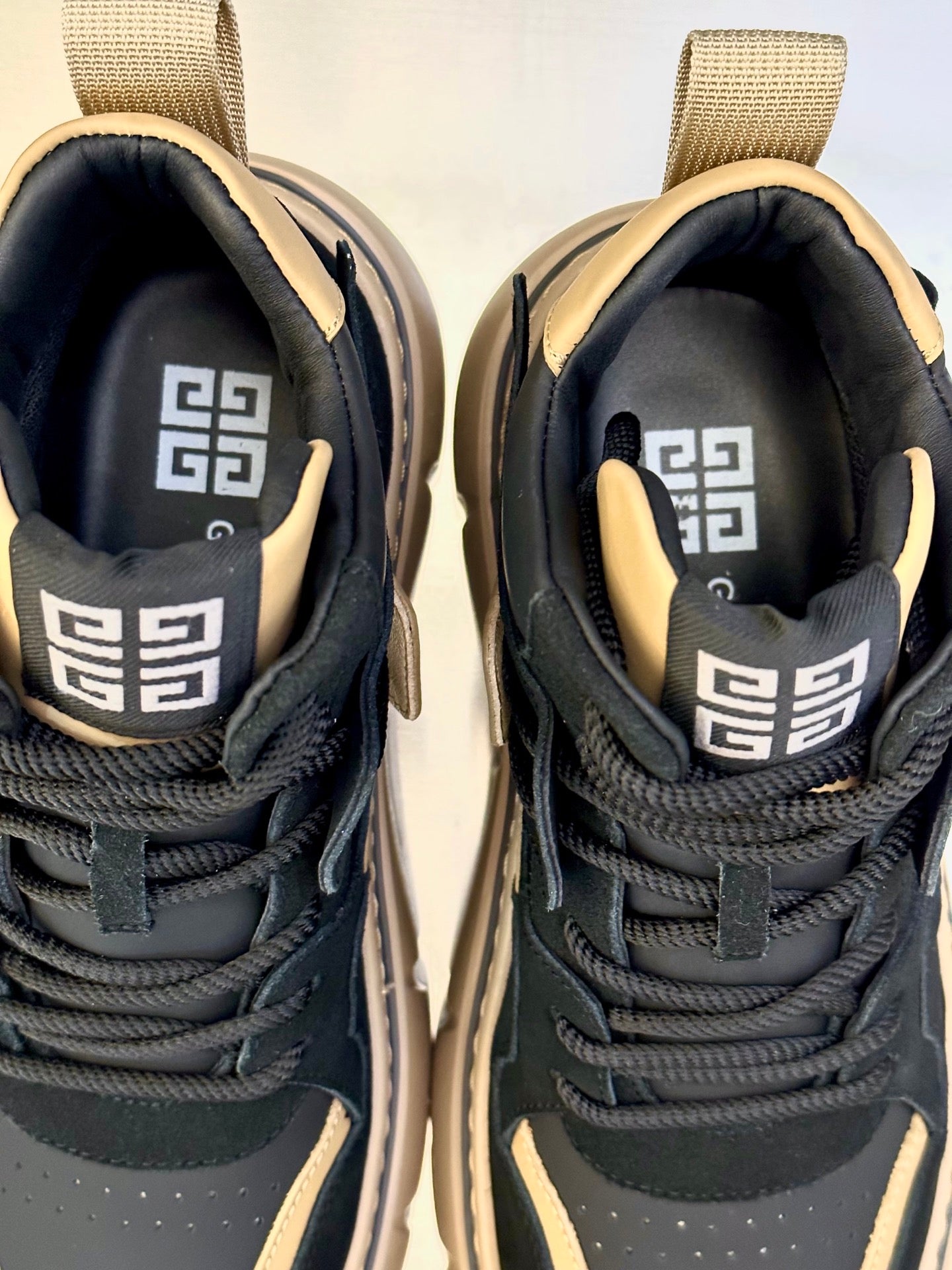 Close-up of black and beige sneaker interior lining with geometric logo on tongue.
