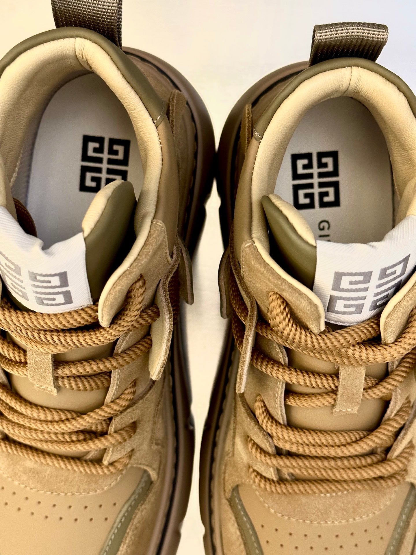 Close-up of olive-brown suede sneakers: lacework, tongue label, and interior logo lining.