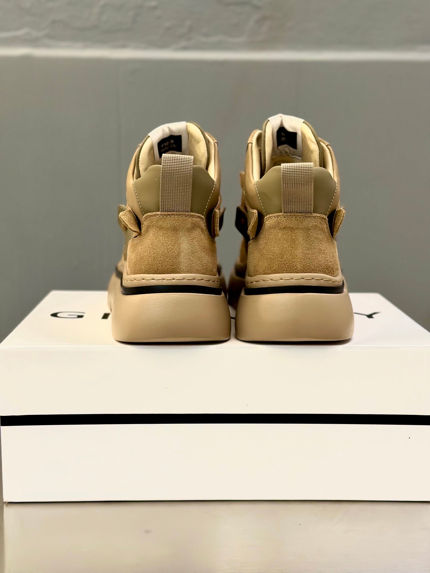 Olive-brown suede sneakers back view with heel tabs and cushioned collars on box.