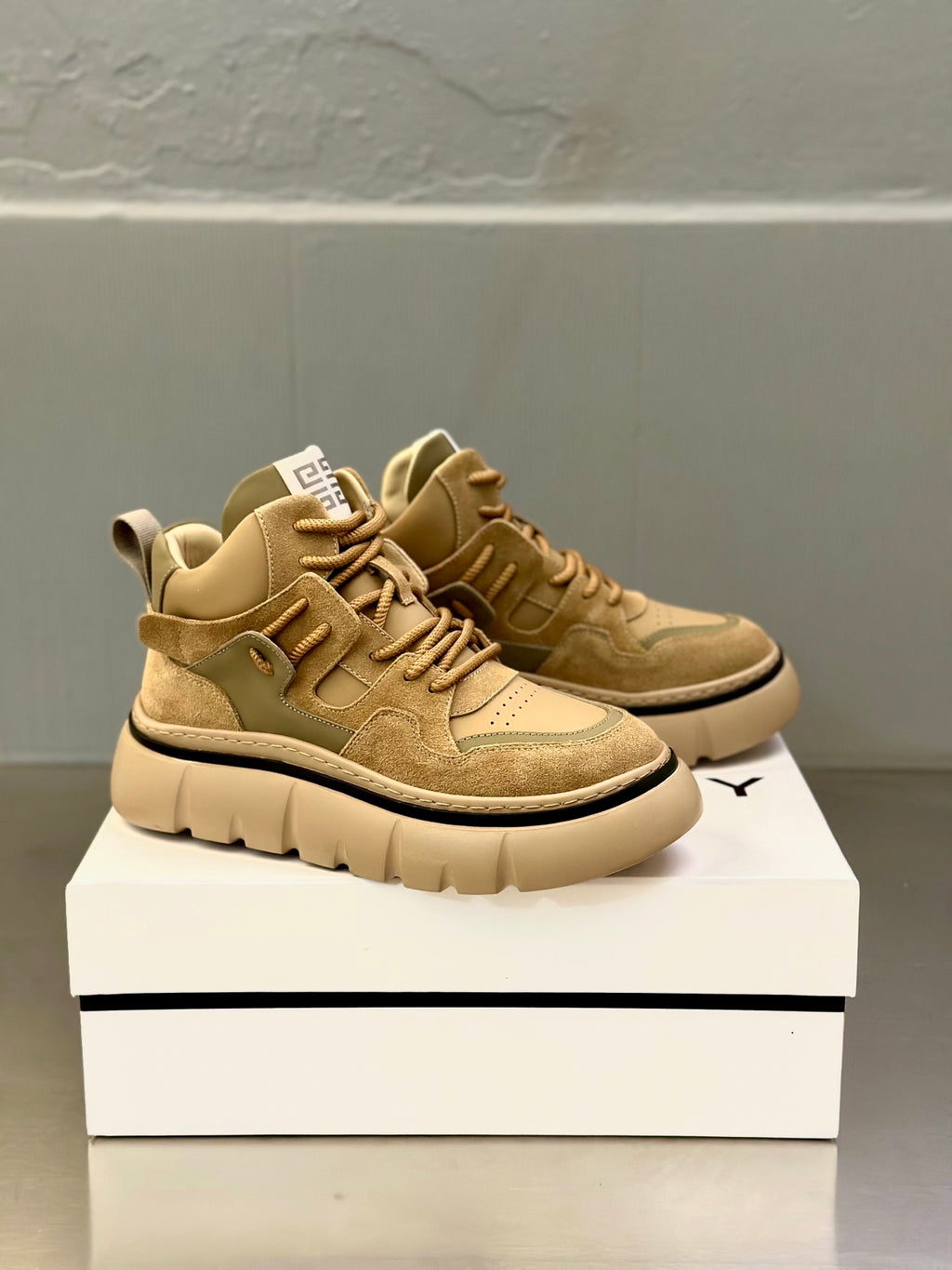 Olive-brown suede sneakers with lace-up front and textured panels, shown in angled view.