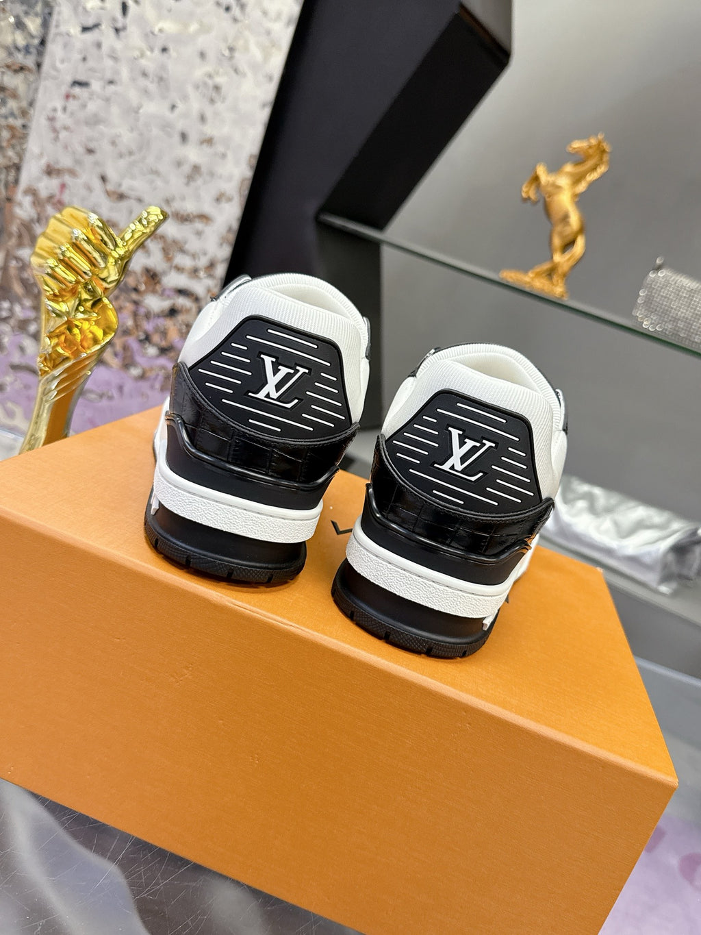 Louis Vuitton ladies sneakers back view, black heel caps and white uppers on orange box.