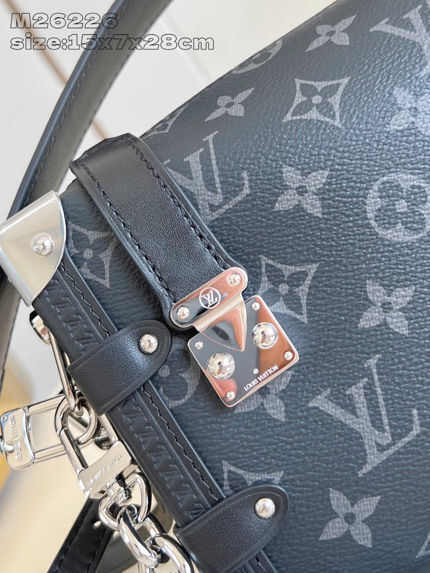 Crossbody bag detail: dark monogram strap, silver hardware, decorative charm