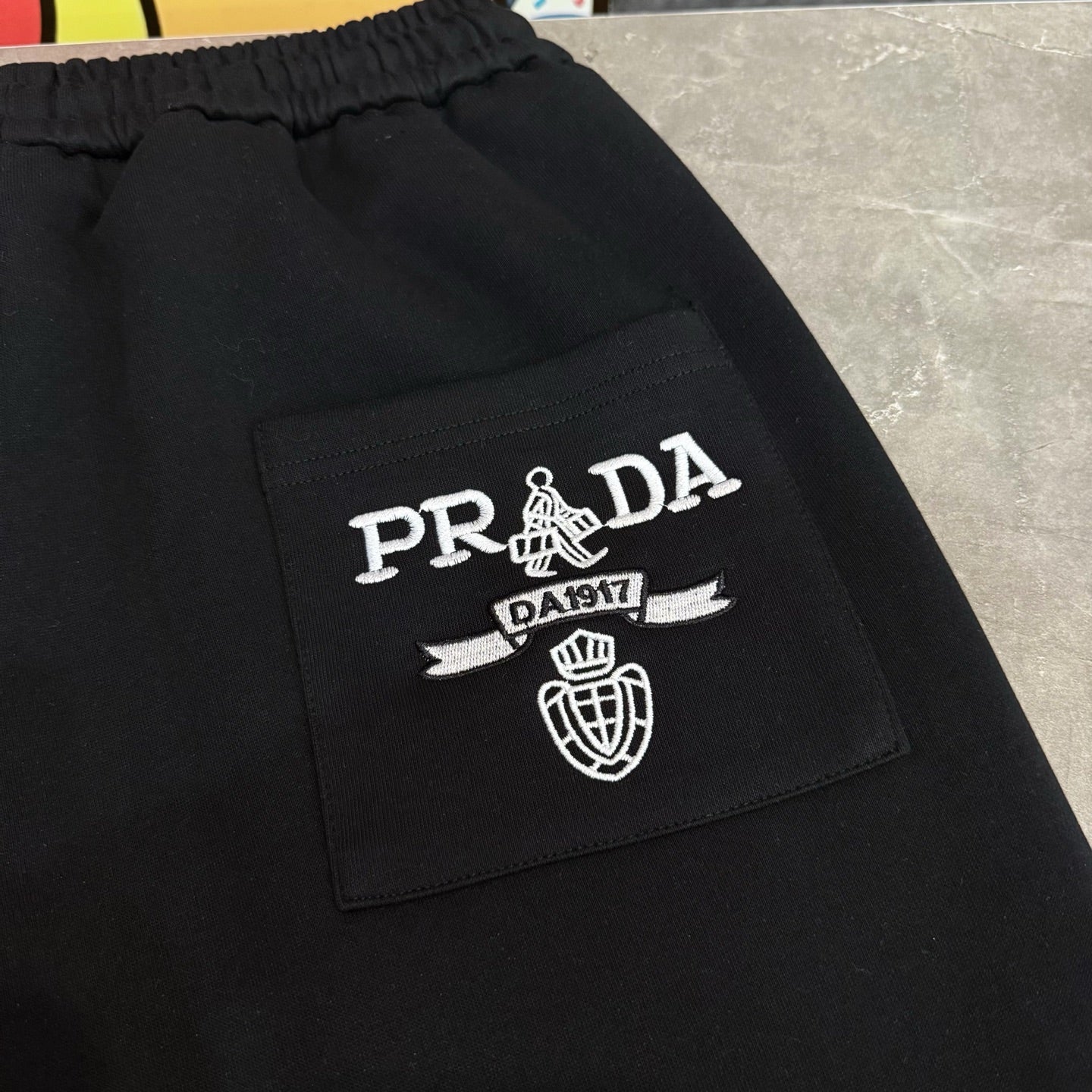 Black Prada pants with embroidered PRADA crest on front pocket area.