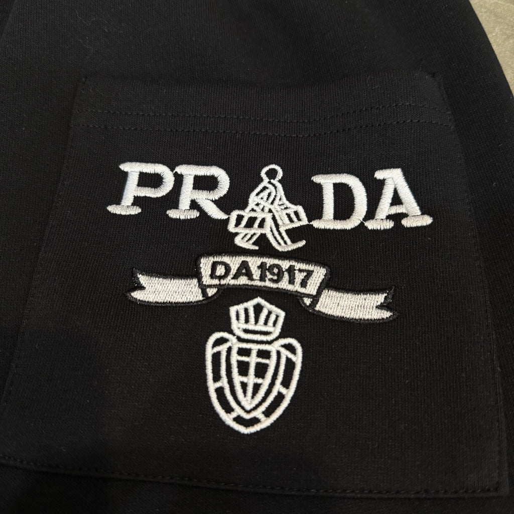 Black Prada pants with embroidered PRADA crest and DA1917 detail.