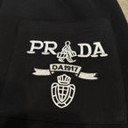 Black Prada pants with embroidered PRADA crest and DA1917 detail.