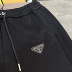 Black Prada pants with front seam detail and triangular PRADA logo patch.