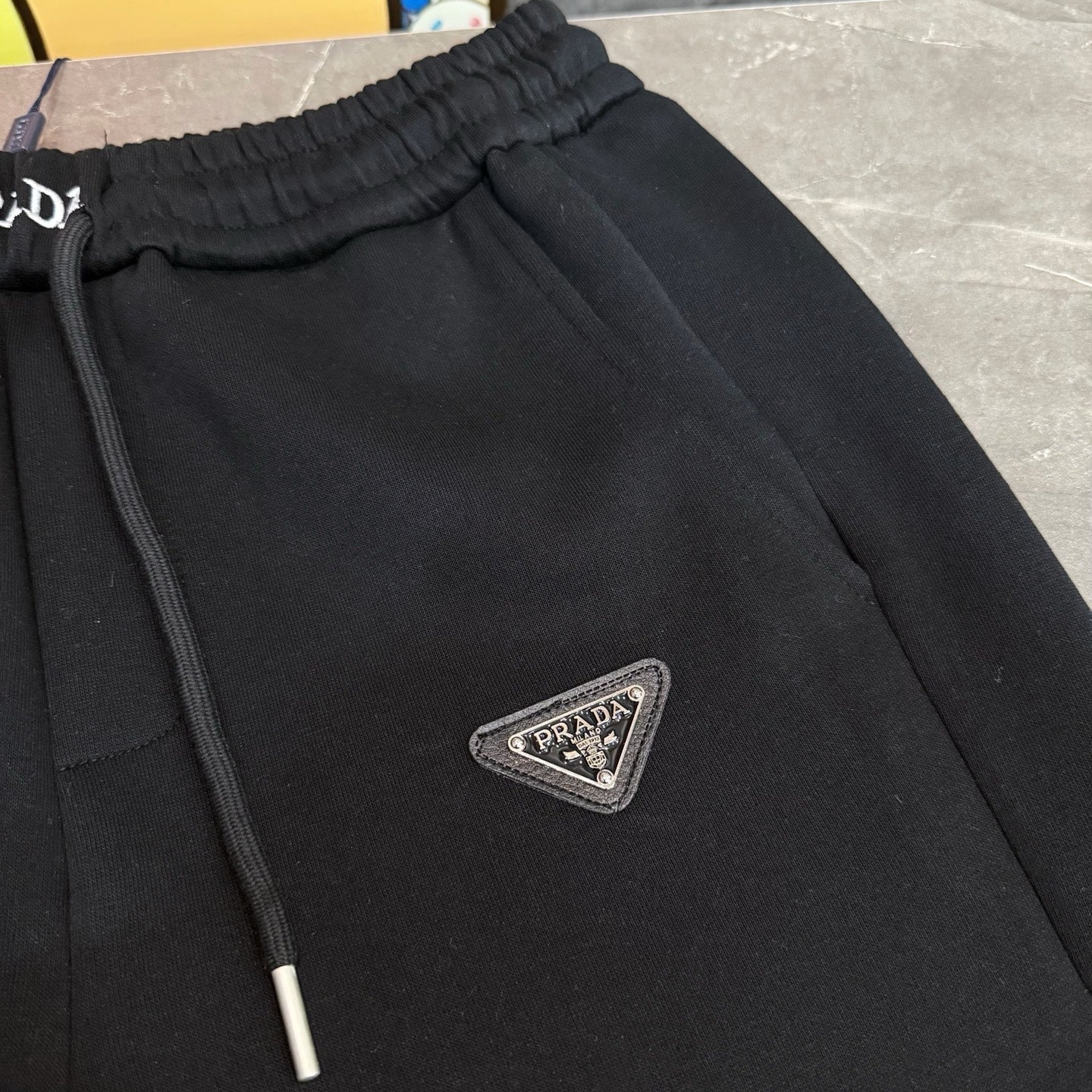 Black Prada pants with front seam detail and triangular PRADA logo patch.