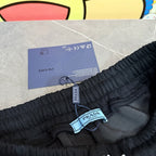 Black Prada pants waistband with attached tags and PRADA label on tie.
