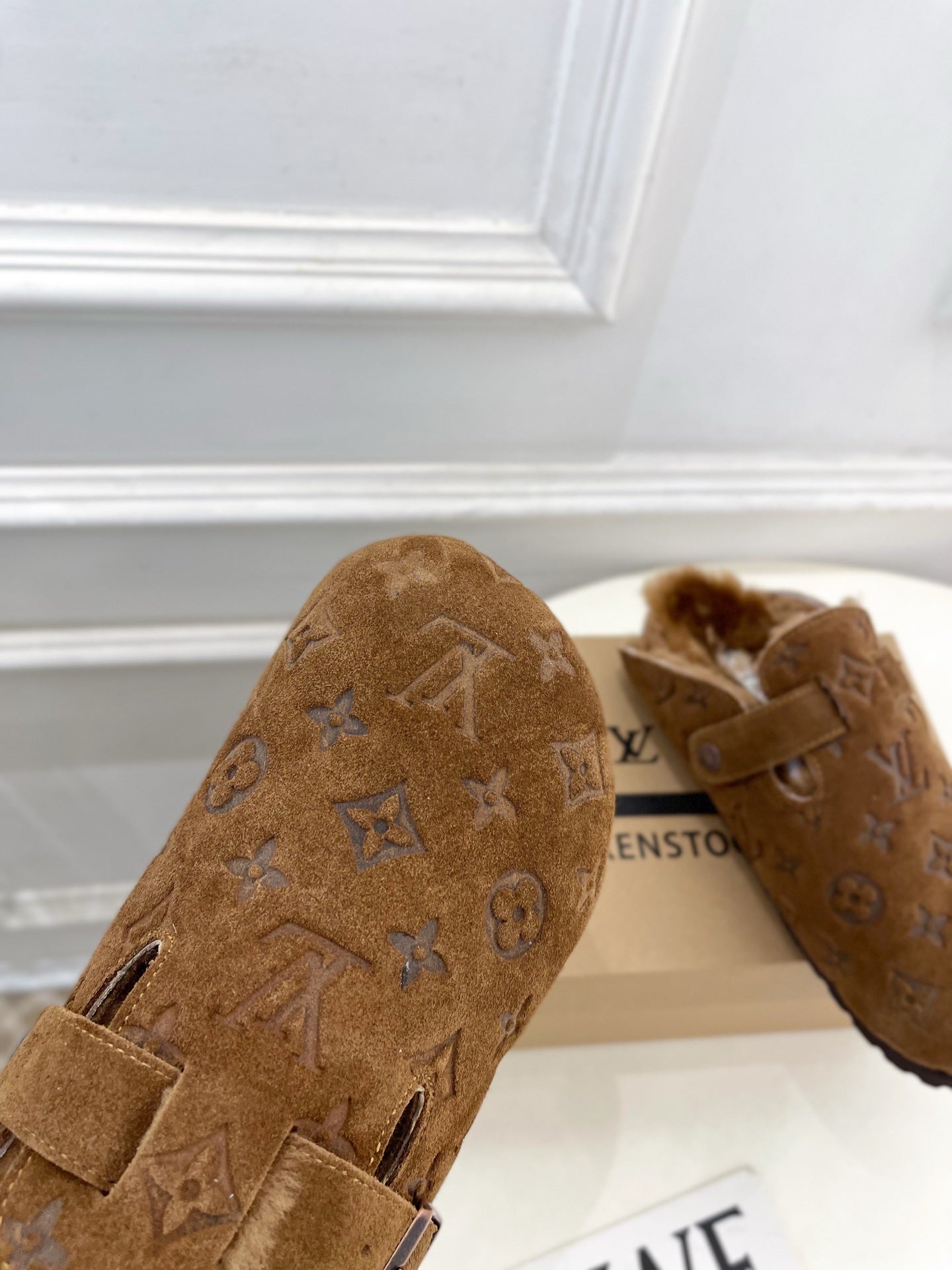 Brown suede sandal with buckle strap and embossed monogram pattern, toe view