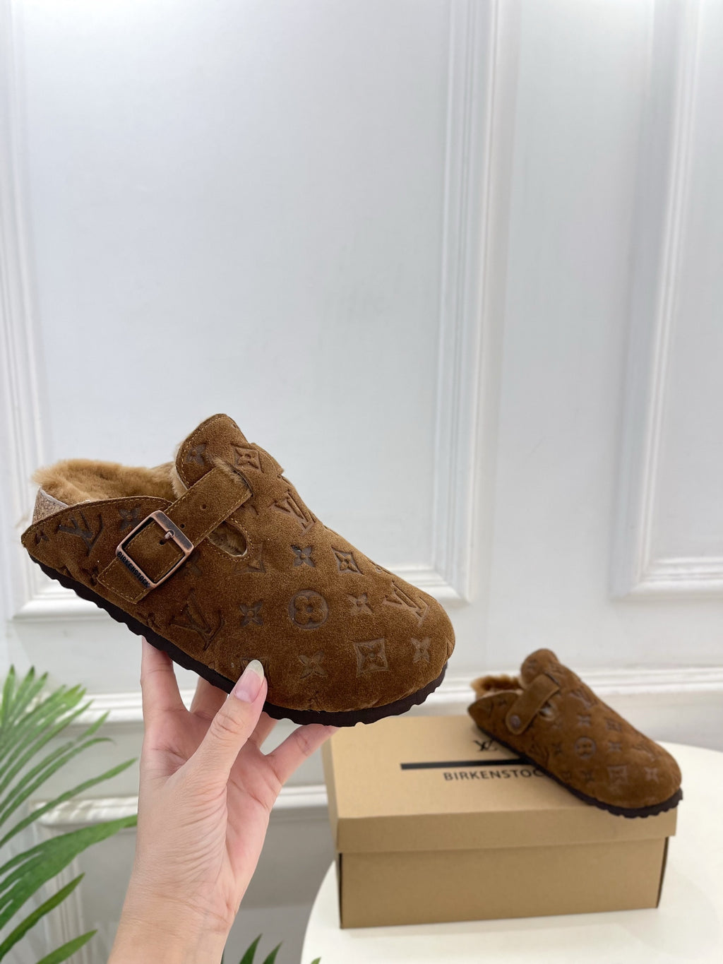 Brown suede slide sandals with buckle strap and shearling lining, side view
