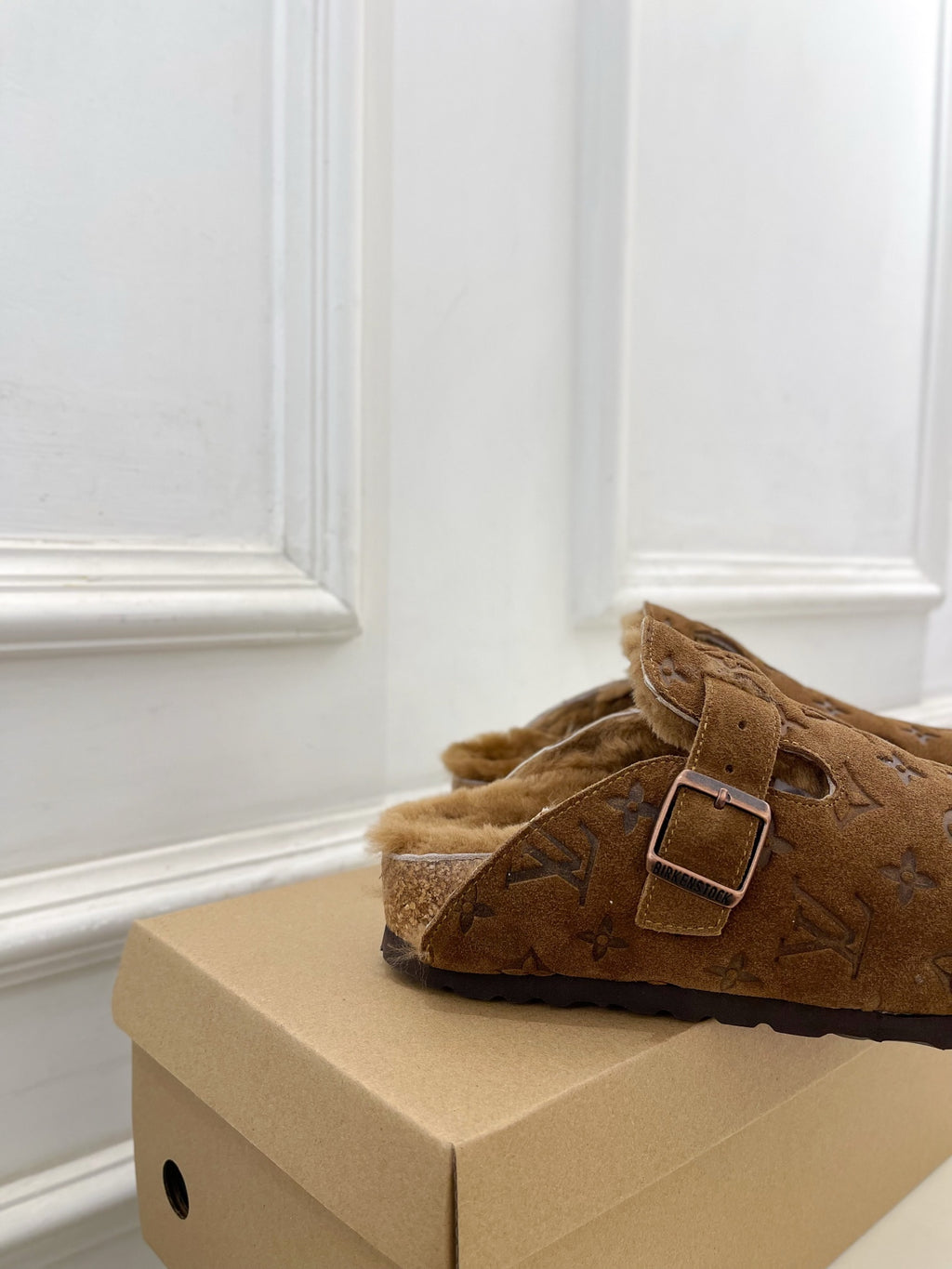Brown suede slide sandals with buckle strap and shearling lining, angled view
