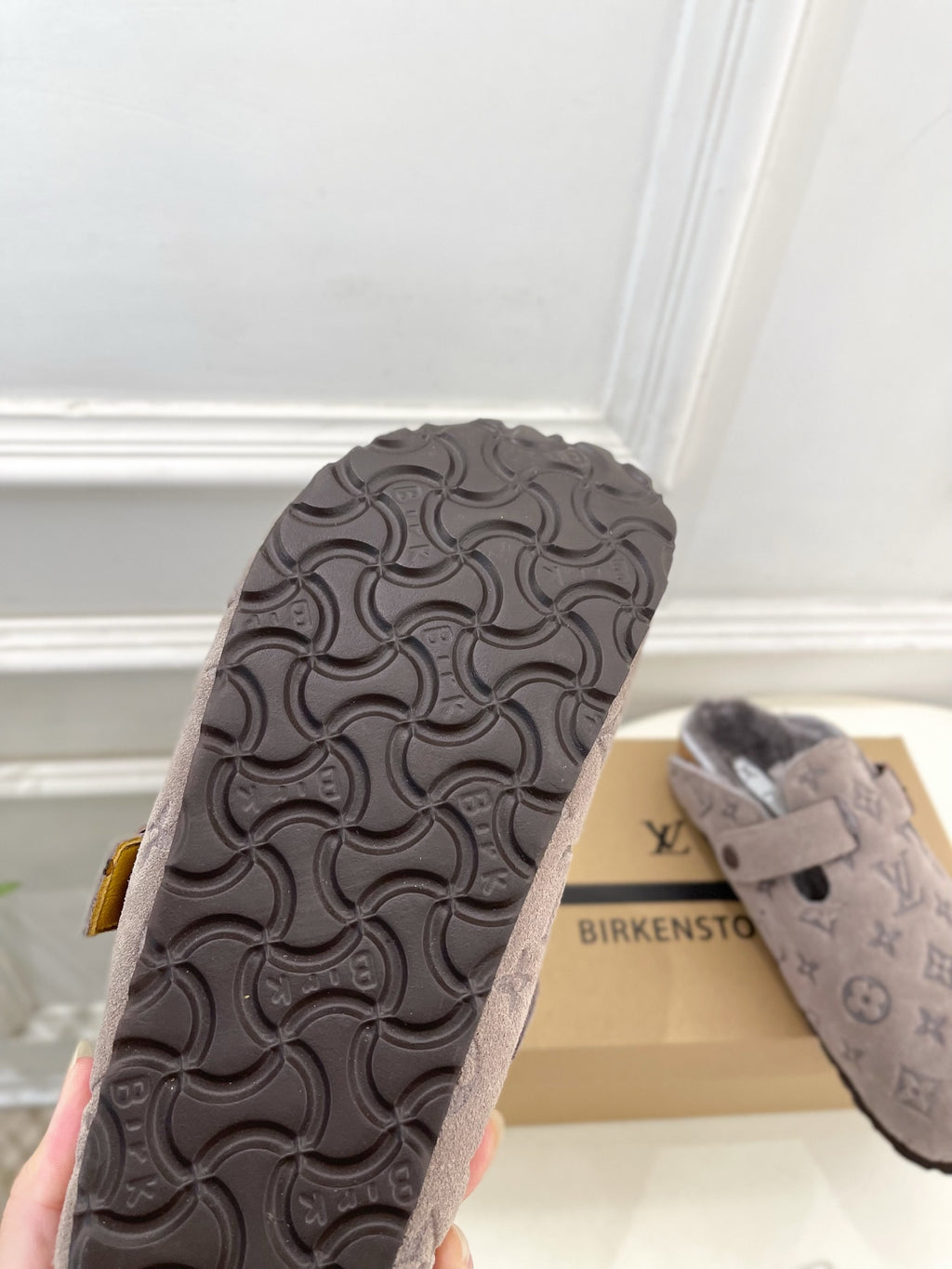 Textured rubber sandal outsole with patterned tread; monogram upper visible behind