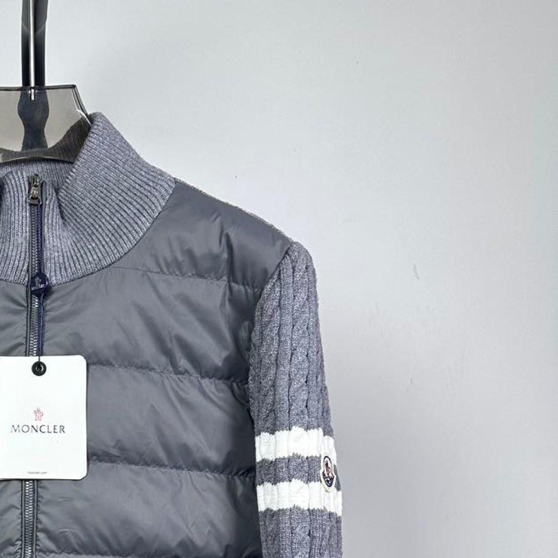 Long puffer jacket front shoulder detail with full zip and gray knit sleeve.