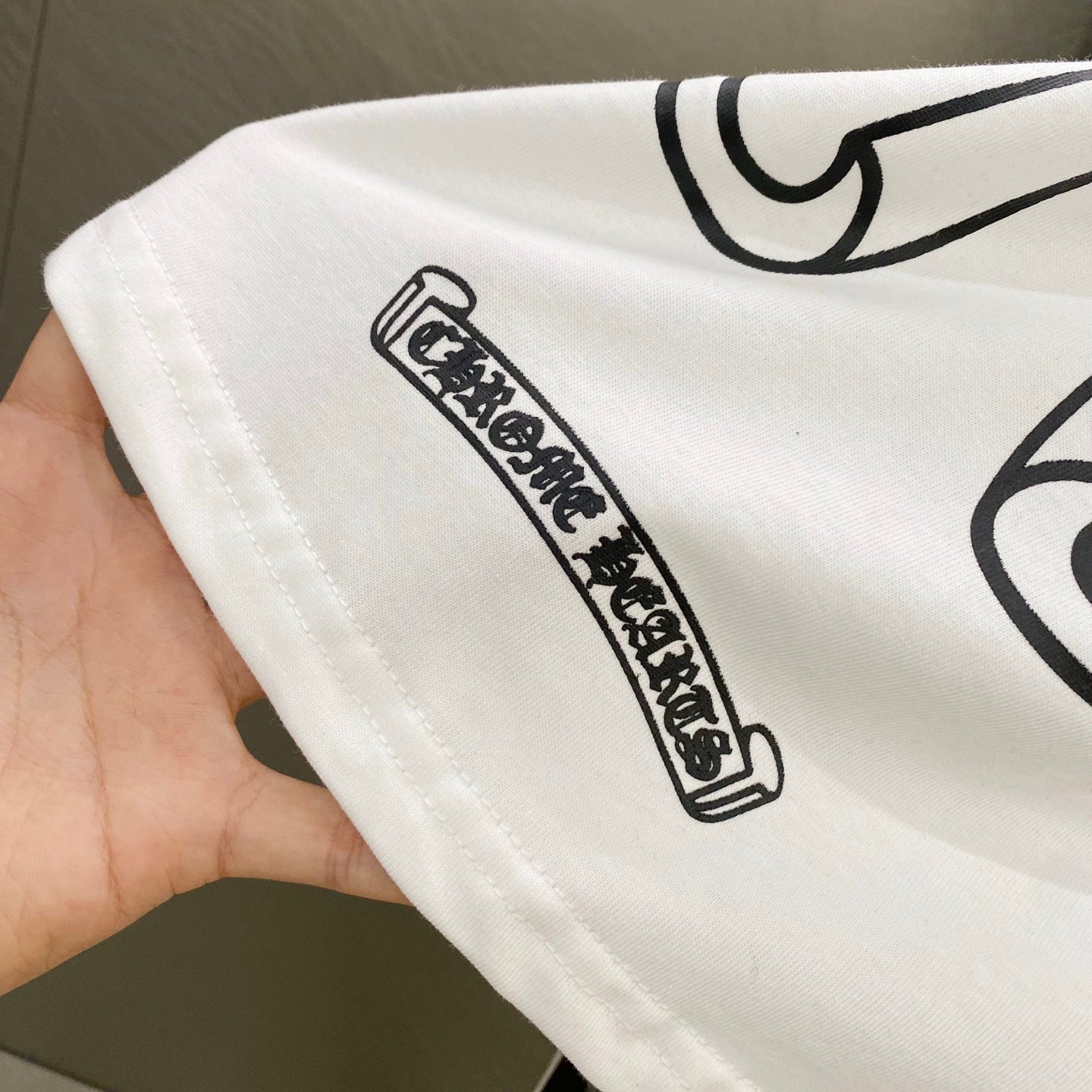 White sleeve cuff with a black logo label text graphic stitched on the fabric.