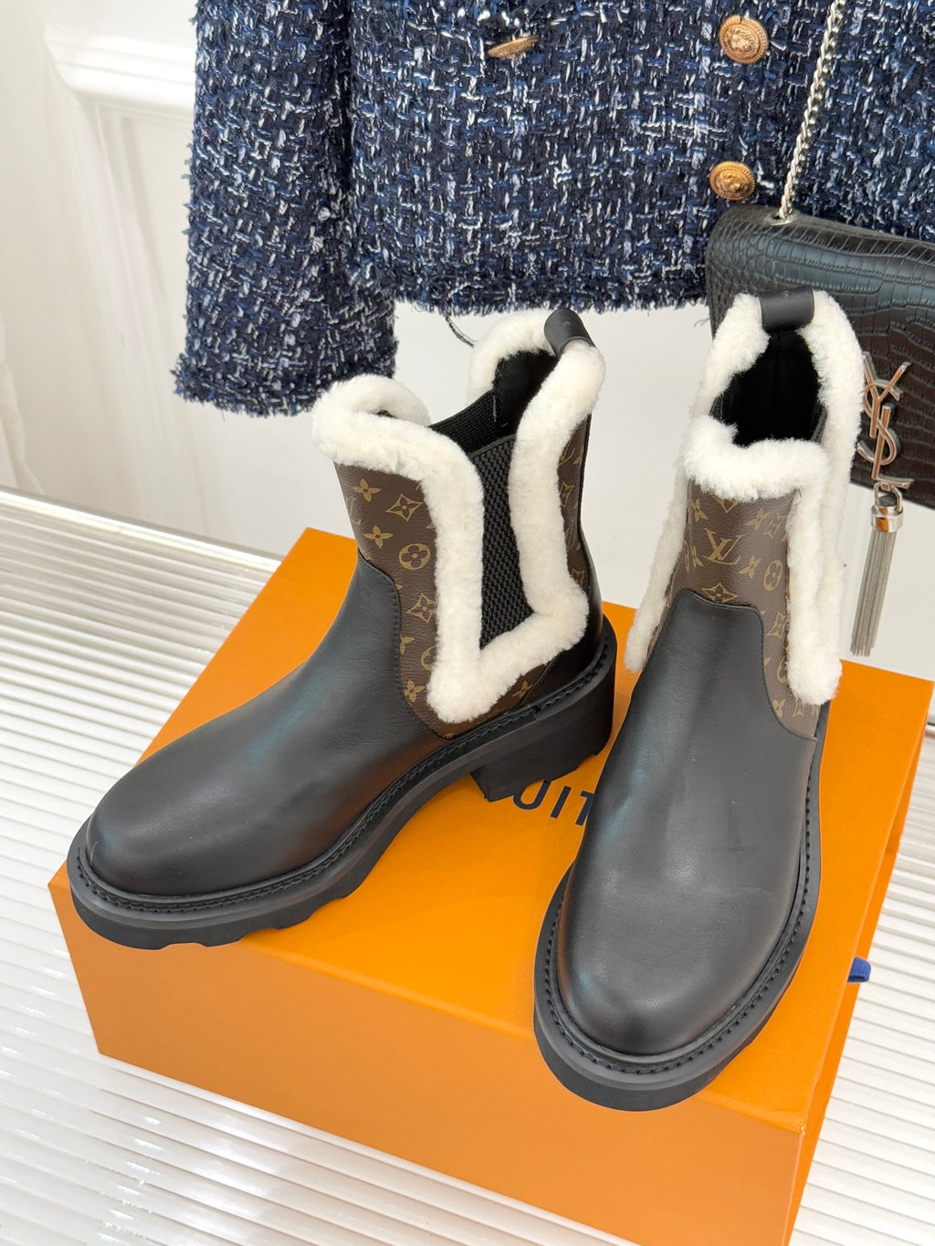 Pair of black ankle boots with white shearling trim and brown monogram side panels