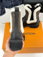 Front view of black ankle boots with white shearling trim and brown monogram panels