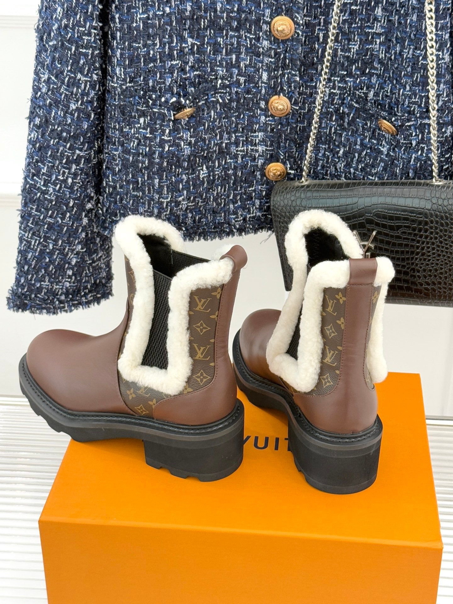 Two brown Louis Vuitton ankle boots with white sherpa cuffs and monogram detailing