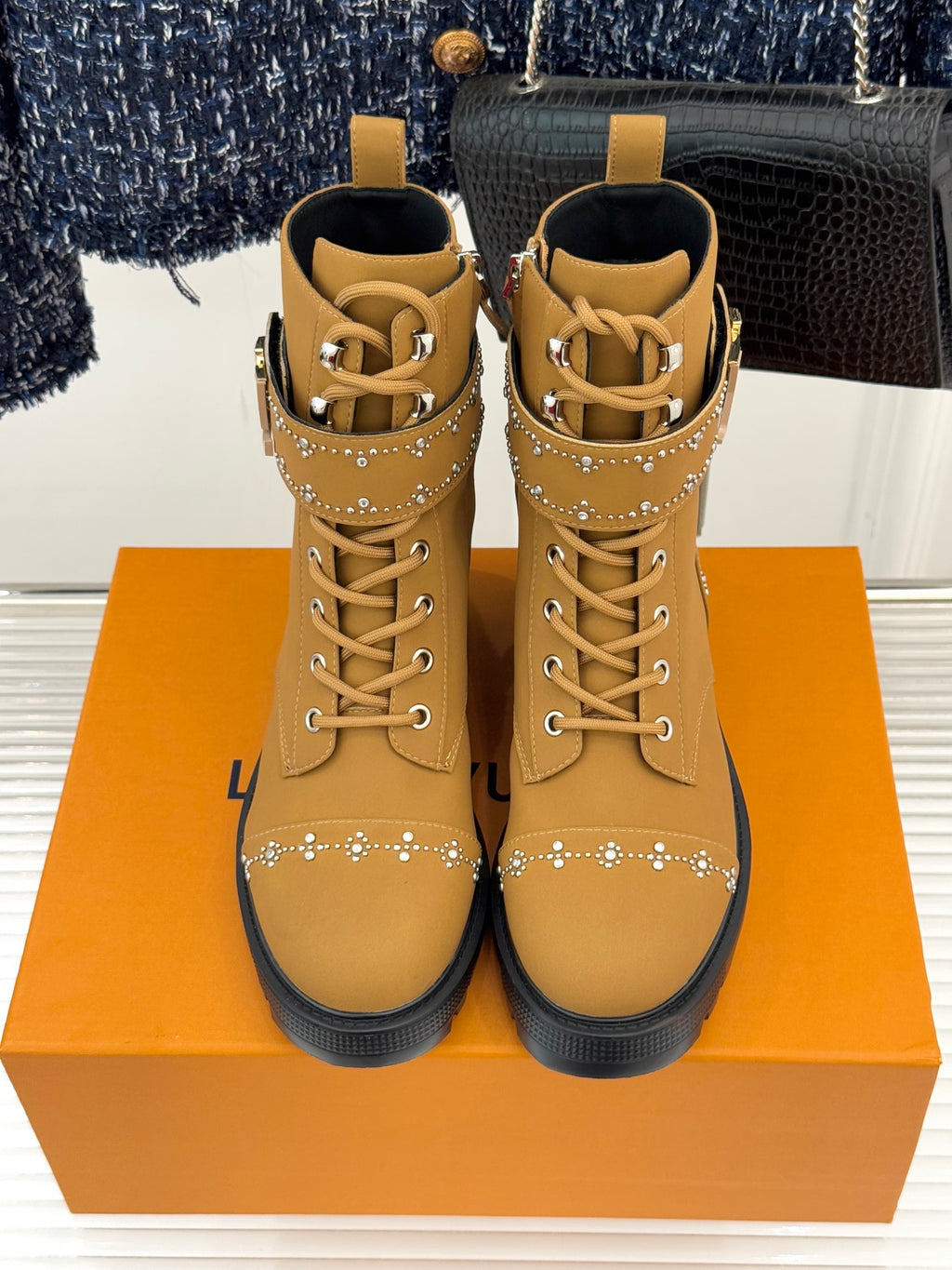 Pair of tan high-top lace-up boots with gold studded straps and chunky tread sole