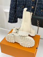 Cream ankle boots with chunky sole tread and side logo, paired on an orange box