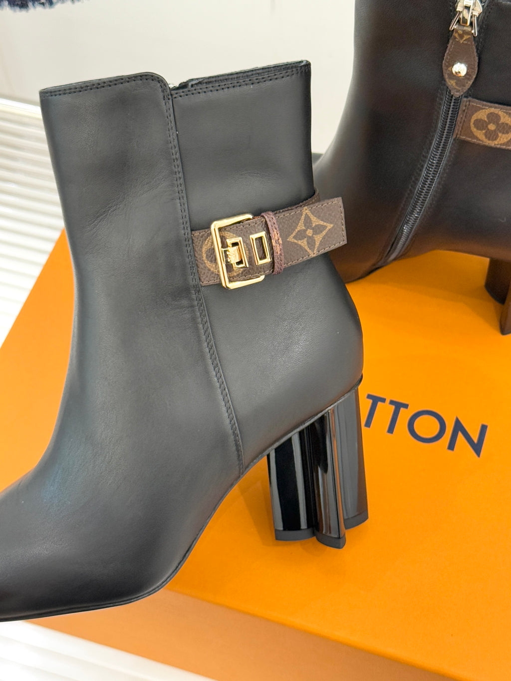 Womens dark leather ankle boot with side zip and logo buckle strap on front.