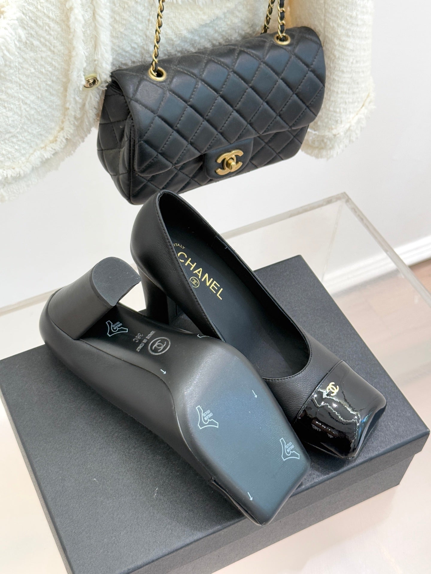 Black Chanel high-heel pumps with patent toe trim and gold logo details on box