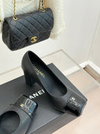 Black Chanel pumps with block heel, glossy toe caps, and gold Chanel emblem