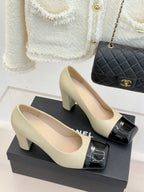 Beige heeled pumps with black patent front strap and gold CC buckle, side view