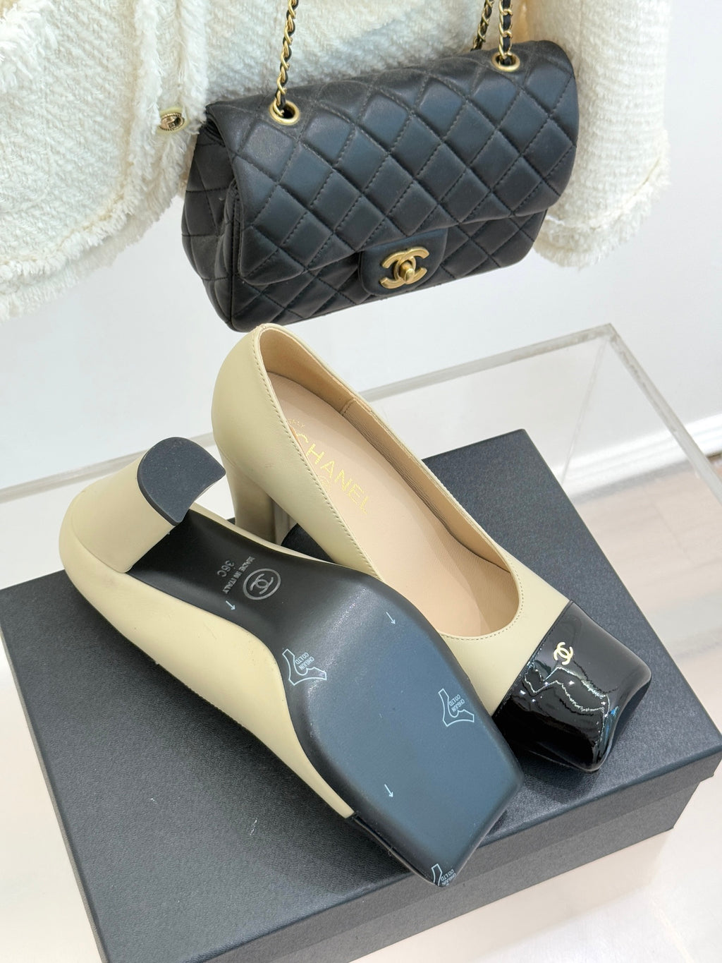 Beige high-heel pumps with black glossy buckle strap and gold CC detail, pair
