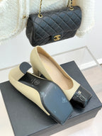 Beige high-heel pumps with black glossy buckle strap and gold CC detail, pair
