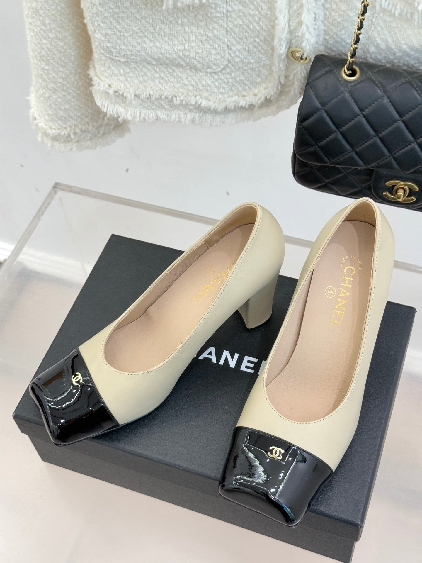 Beige high-heel pumps with black glossy strap and gold CC buckle, pair