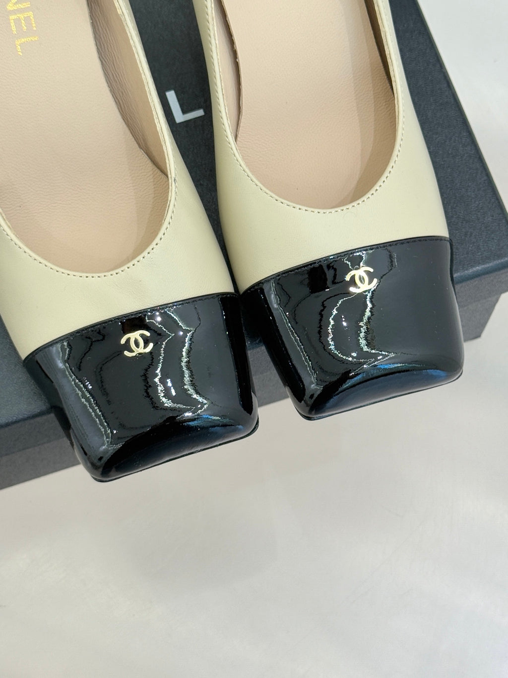 Beige pumps with black patent toe strap and gold CC logo, close-up