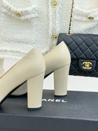 Beige heeled pumps with black patent toe straps and gold CC buckle, close side