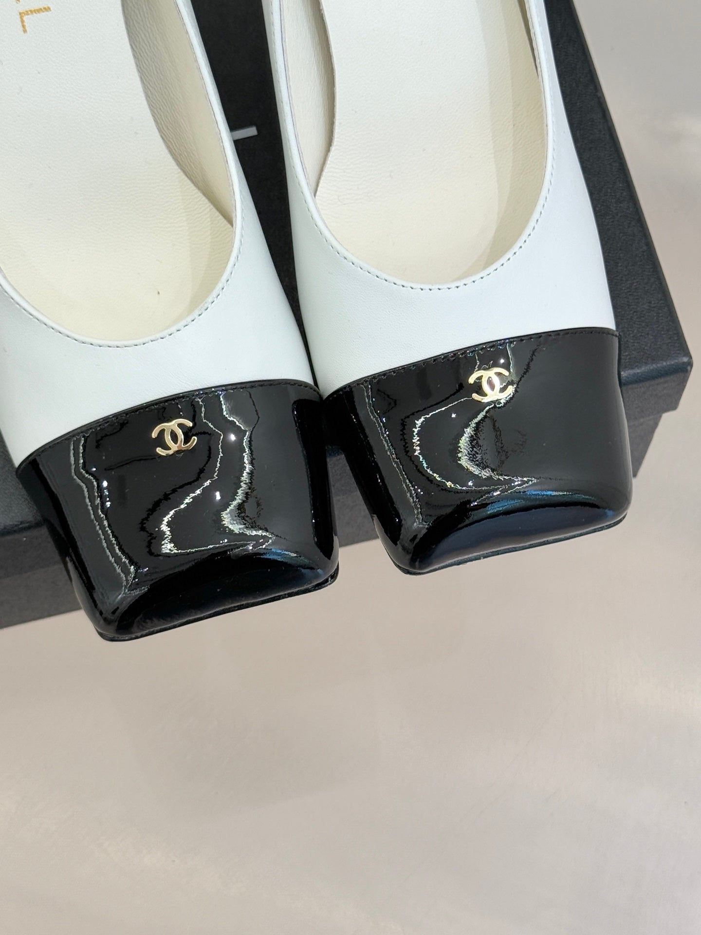 Close-up of women’s Chanel white pumps with glossy black patent toe caps