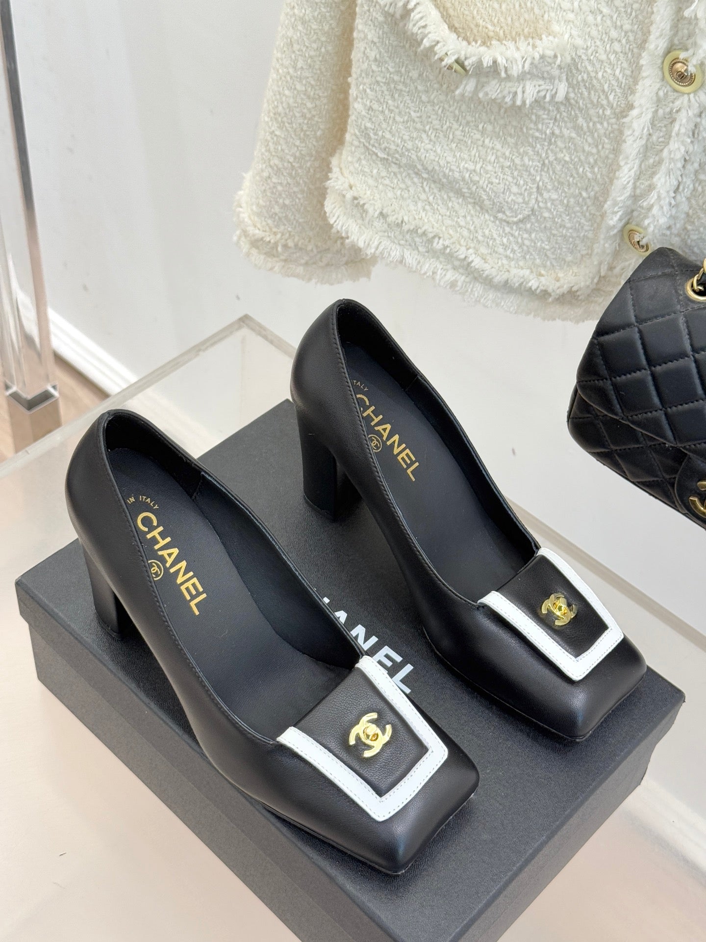 Pair of black heeled mules with white-trim buckle and gold CHANEL logo