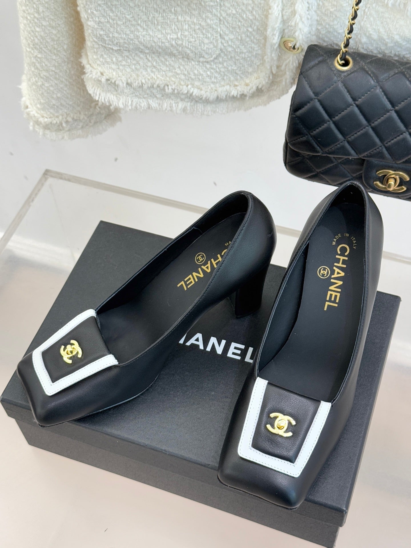 Black heeled mules with white-trim buckle, gold emblem, and CHANEL text