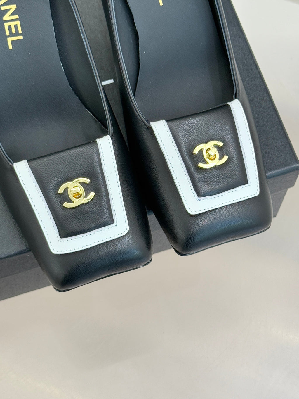 Black heeled mules close-up of white-trim buckle with gold CC emblem