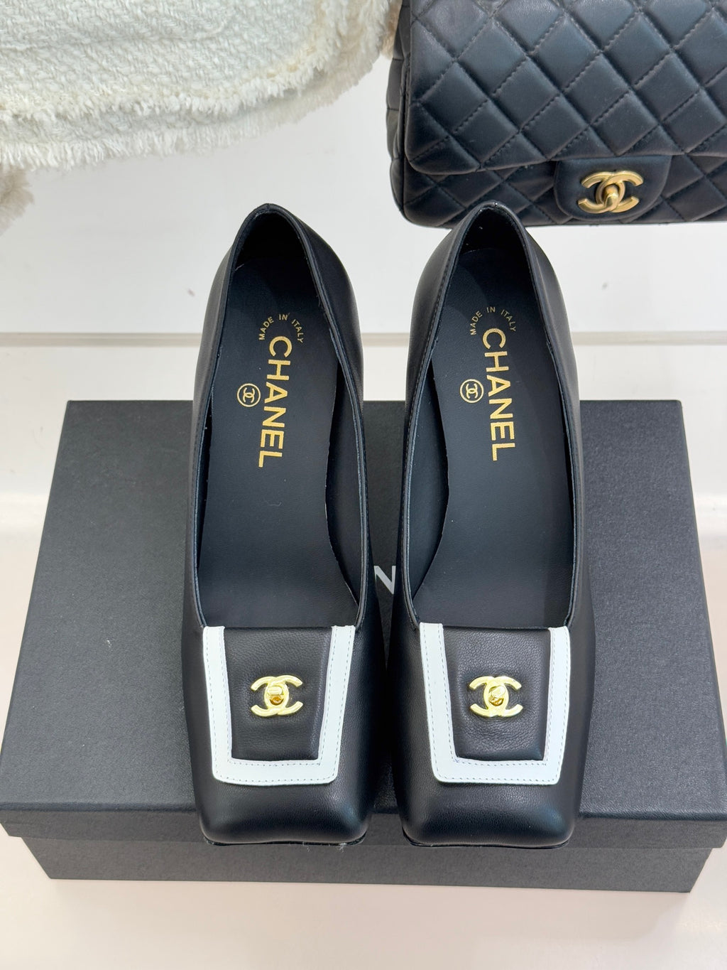 Black heeled mules, side view, with white-trim buckle and gold CHANEL branding