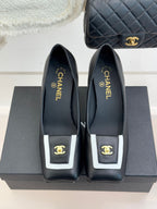 Black heeled mules, side view, with white-trim buckle and gold CHANEL branding