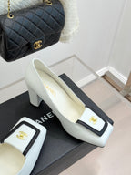 White leather block-heel pumps with black-trimmed front and gold logo on emblem