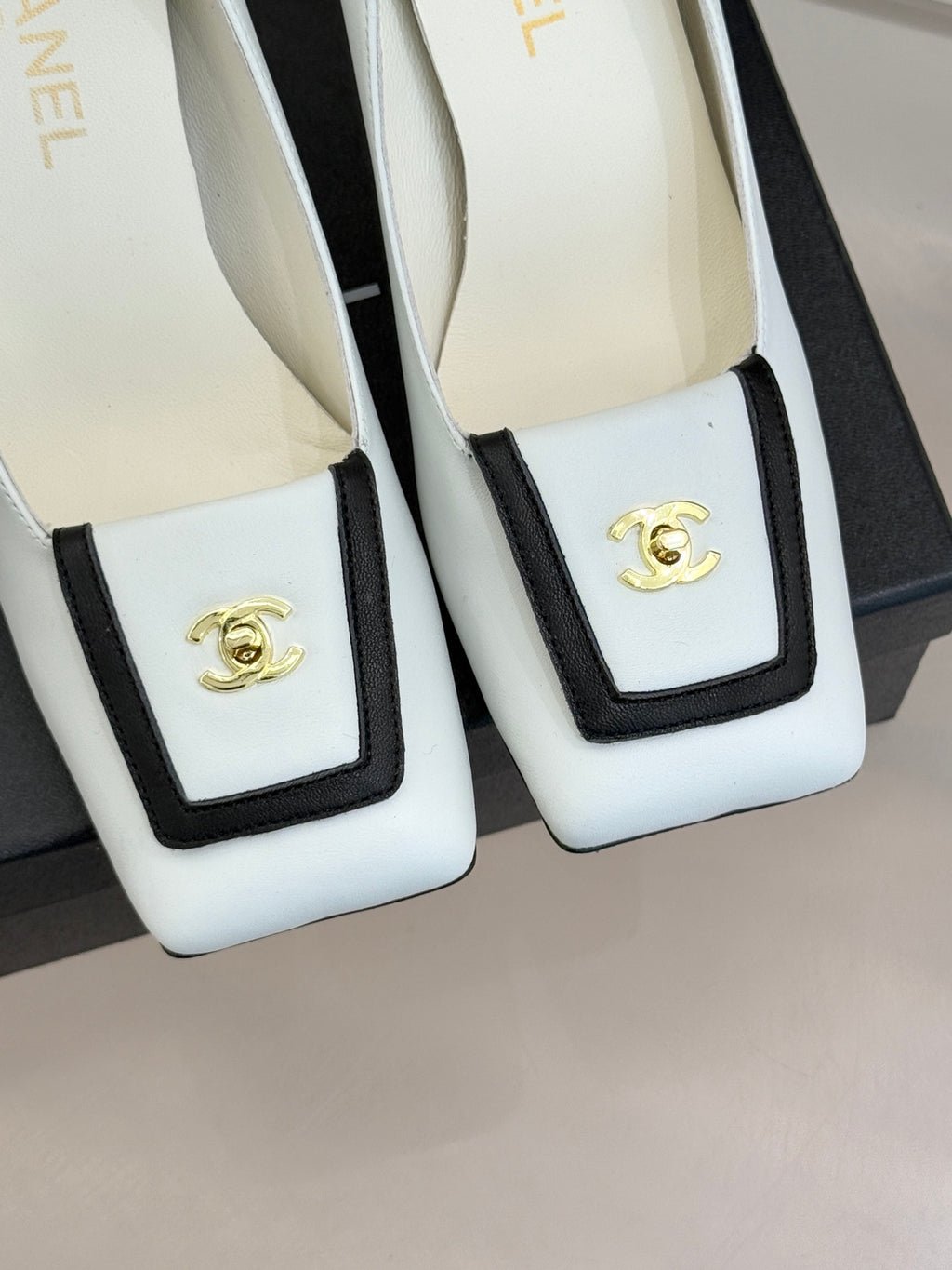 White leather pumps with black-trimmed square front and gold logo emblem detail
