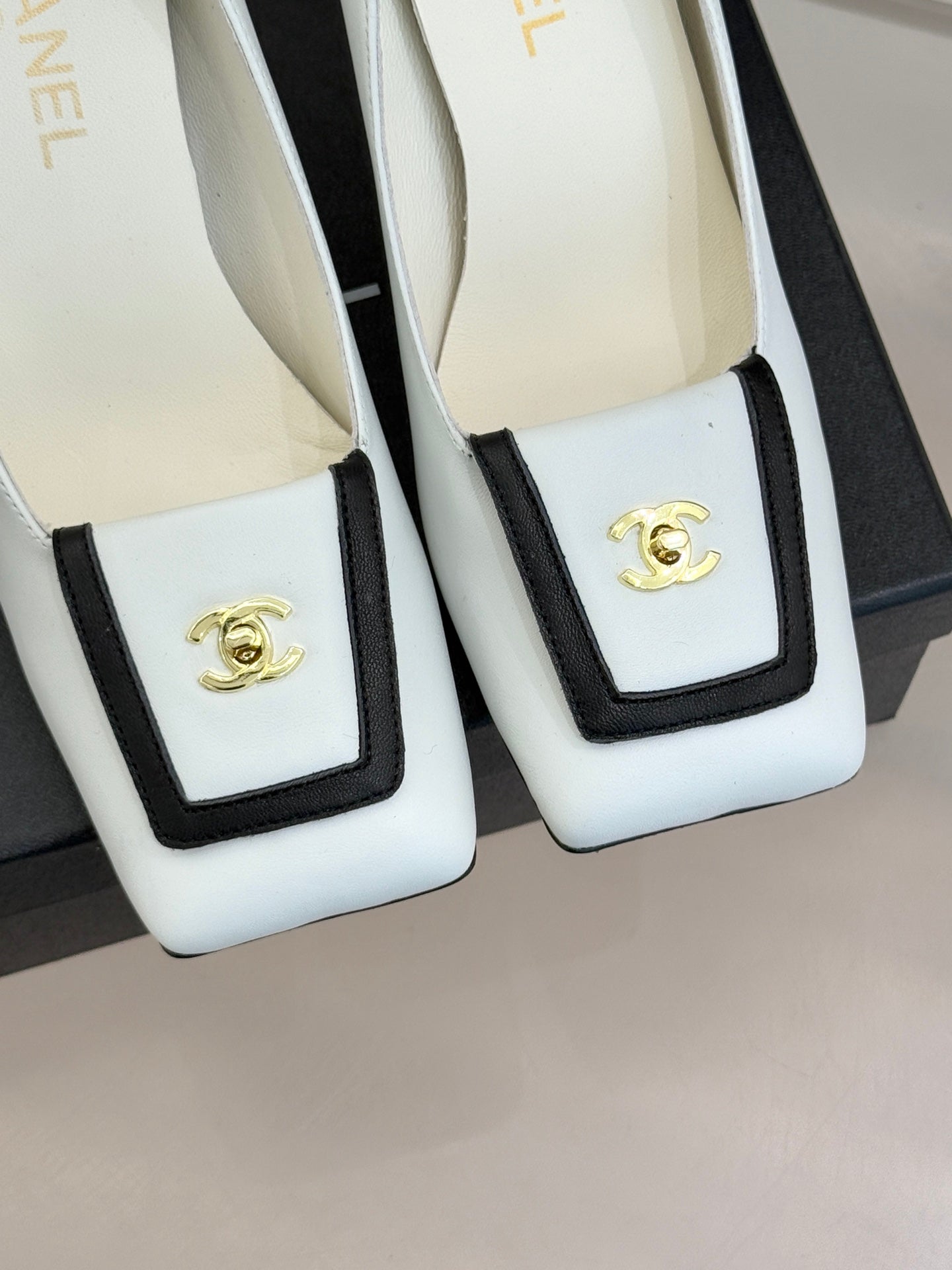 White leather pumps with black-trimmed square front and gold logo emblem detail
