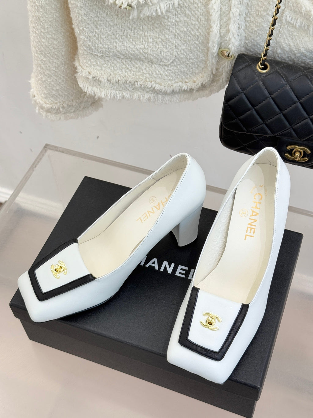 White leather block-heel pumps with black trim, gold logo plaque, and low heel