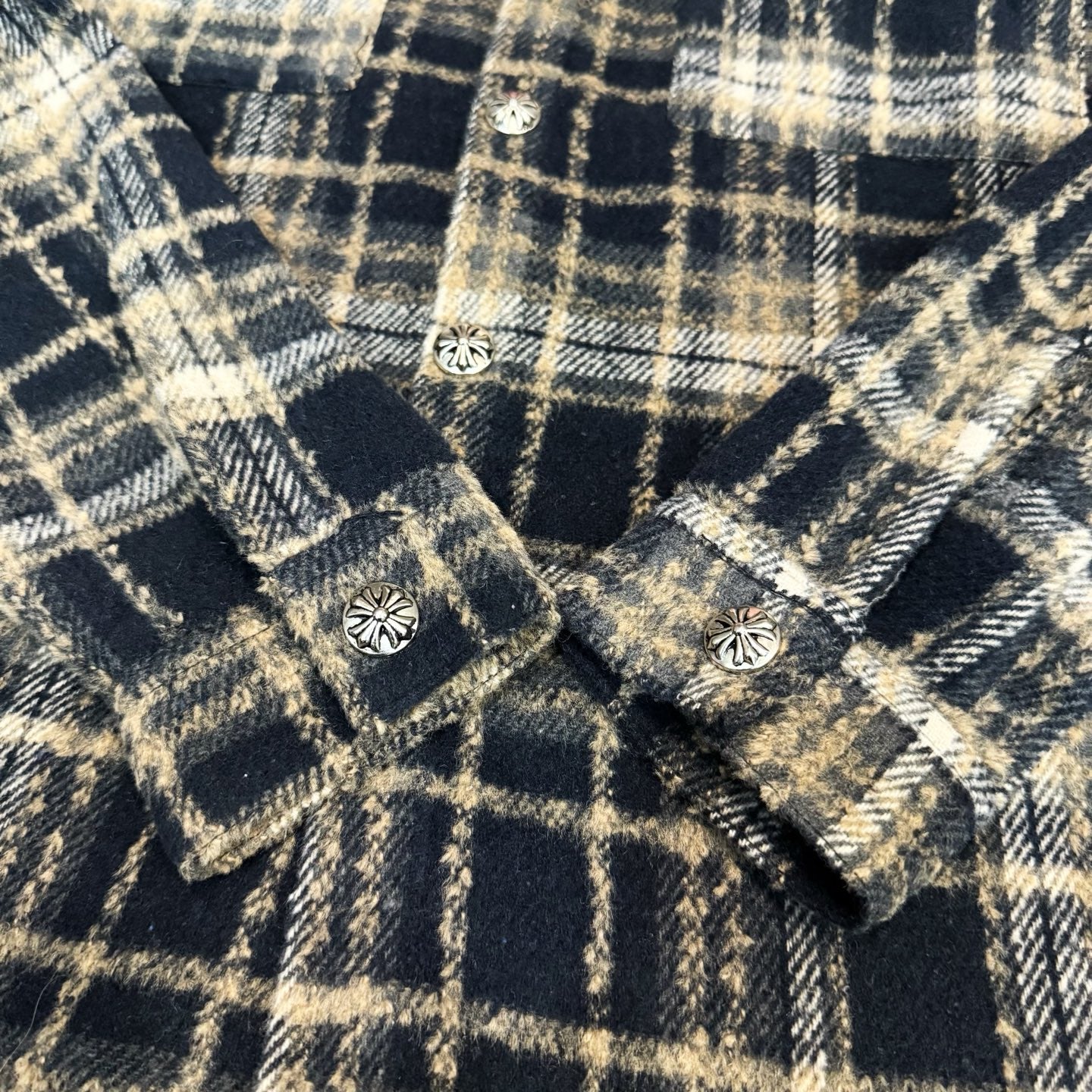 Close-up of navy-and-cream plaid long-sleeve shirt with decorative buttons near seams