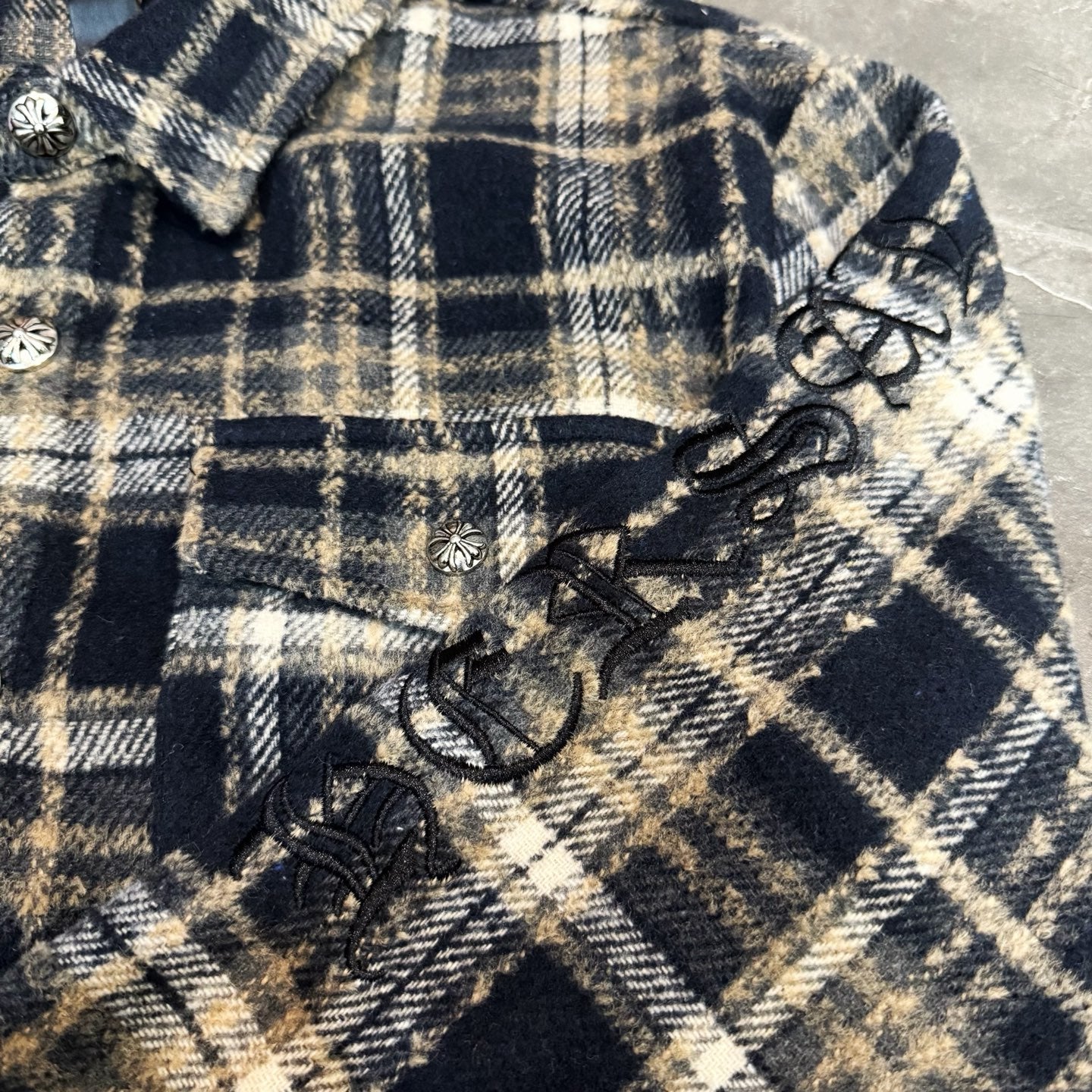Close-up of navy-and-cream plaid sleeve with bow-like trim and decorative buttons
