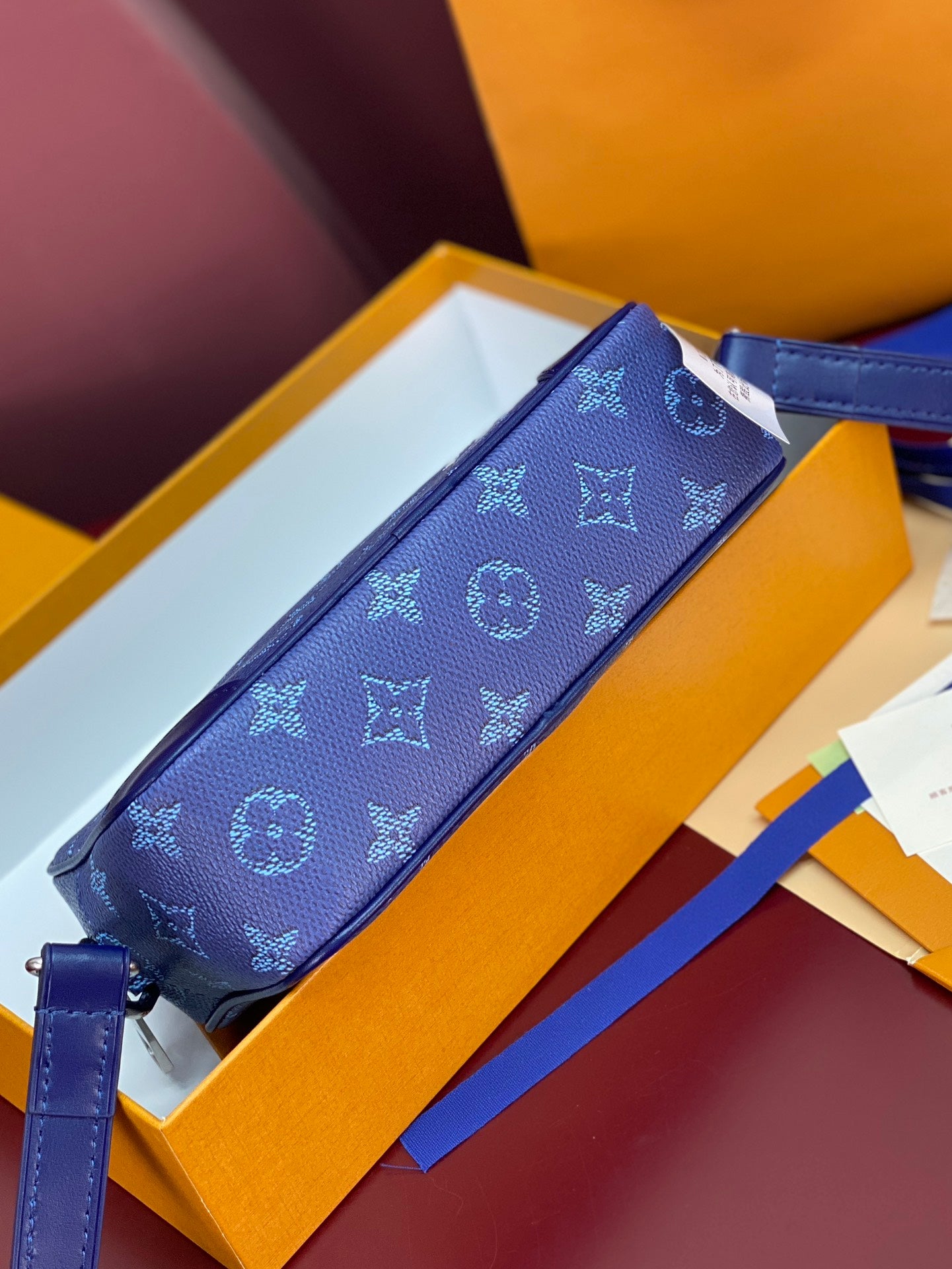 Blue monogram crossbody bag lying on box lid with adjustable strap