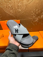 Handheld view of Hermes slide sandals, light blue embossed strap and dark sole