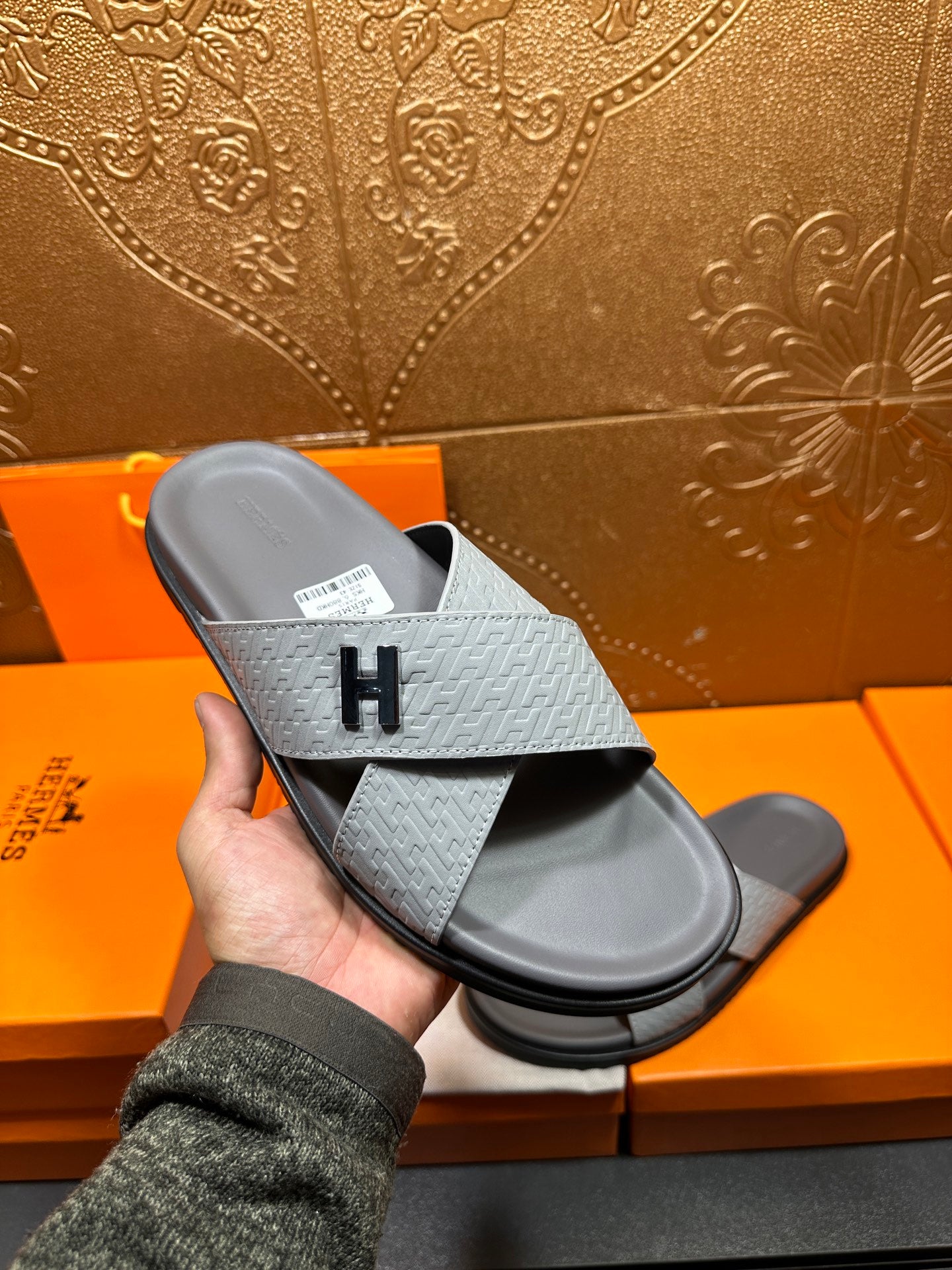 Handheld view of Hermes slide sandals, light blue embossed strap and dark sole