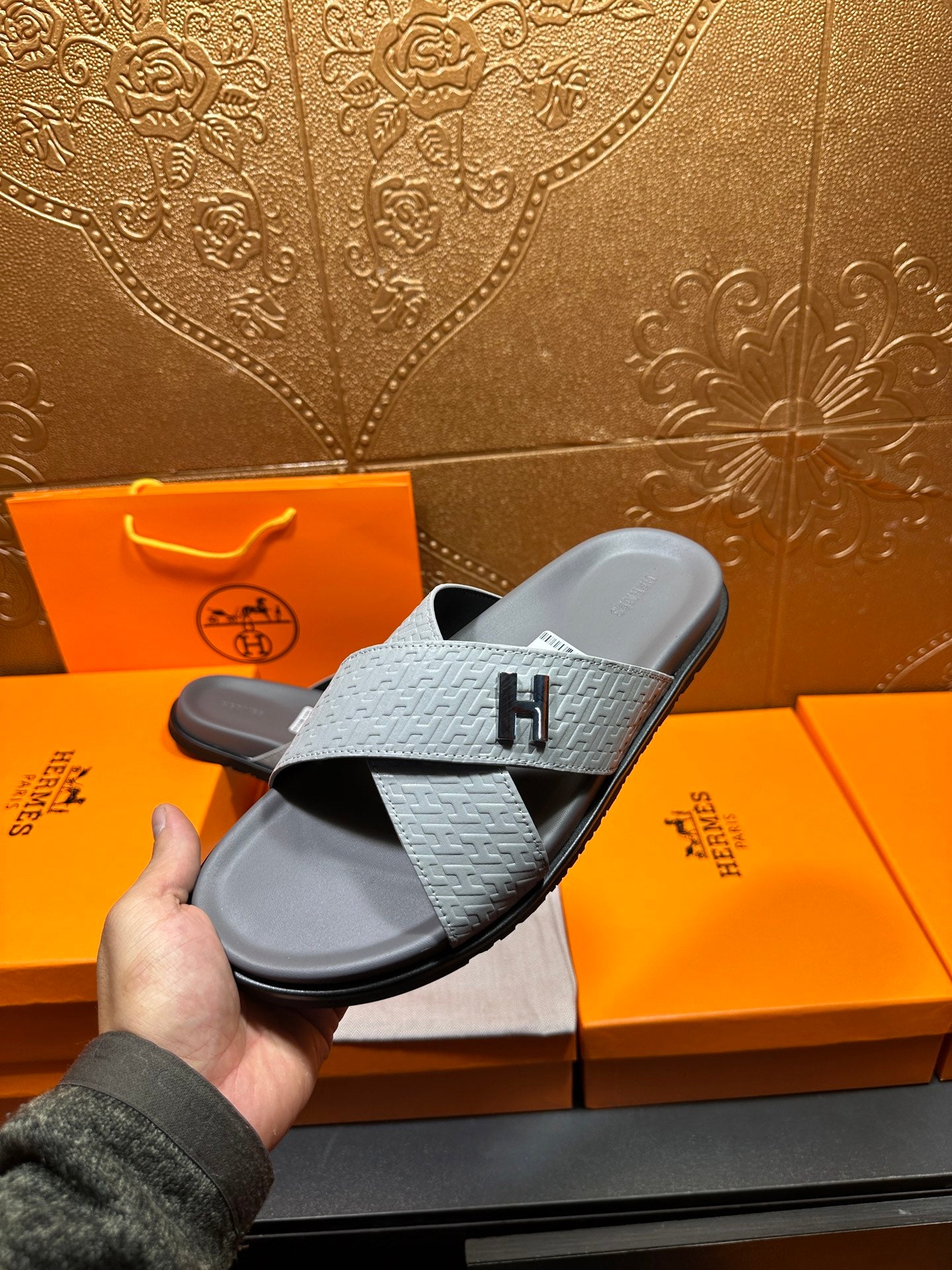 Hermes slide sandals held in hand, light blue embossed straps and dark rubber sole